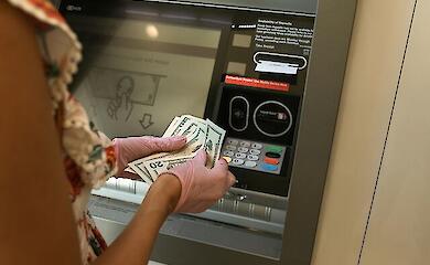 Женщина в перчатках пересчитывает деньги у банкомата