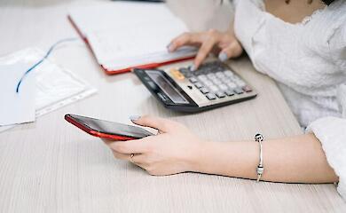 Жінка перевіряє інформацію в телефоні з калькулятором, ілюстративне фото