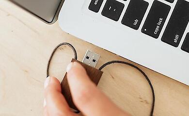 Рука підключає USB-пристрій до роз'єму відкритого ноутбука.