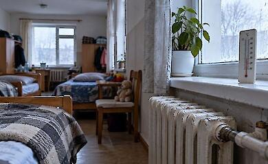 Холодная комната места временного проживания с кроватями, старым радиатором и термометром у окна